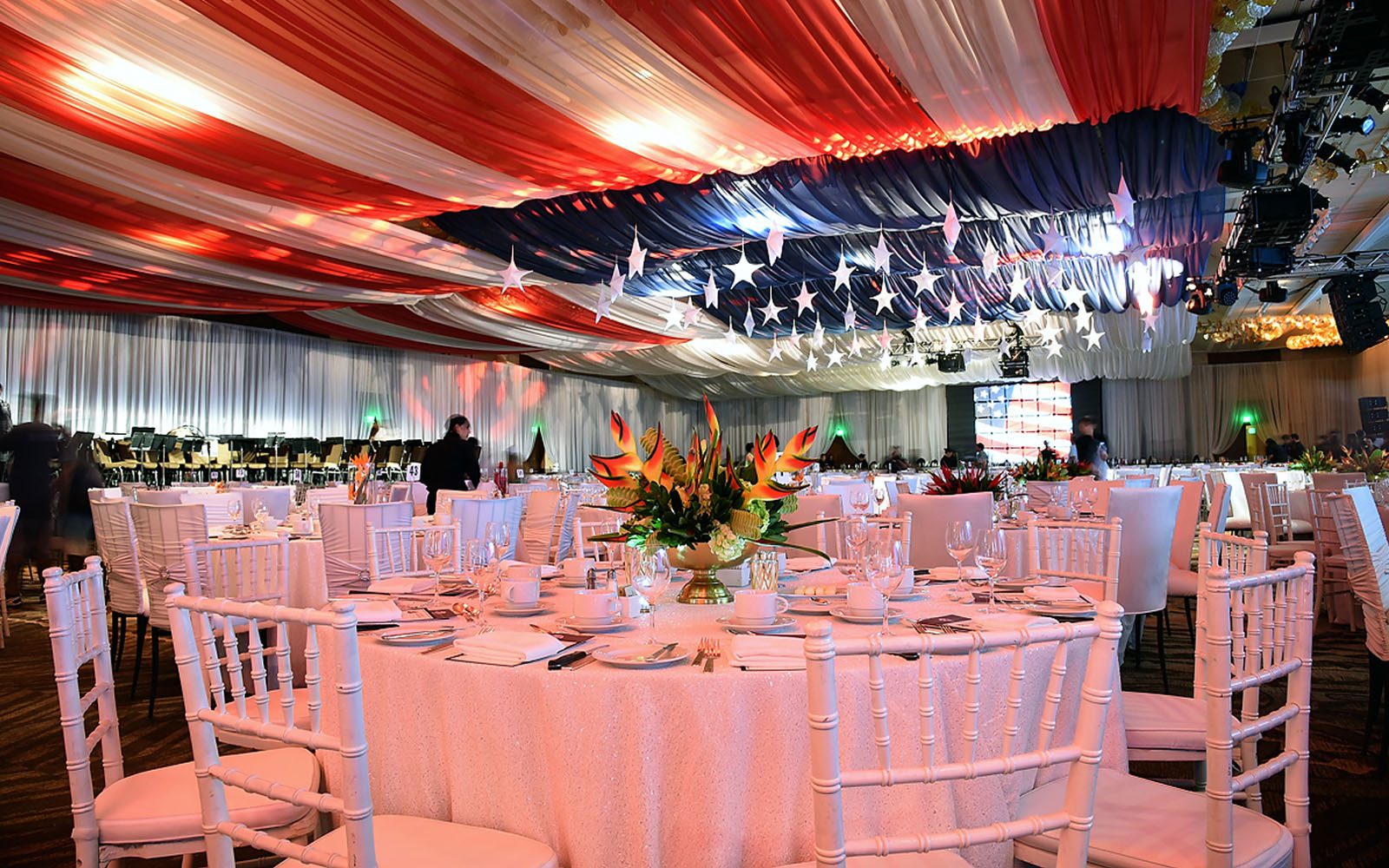 America Flag draped above ceiling in the Coral Ballroom with white tables and chairs set up for the event.