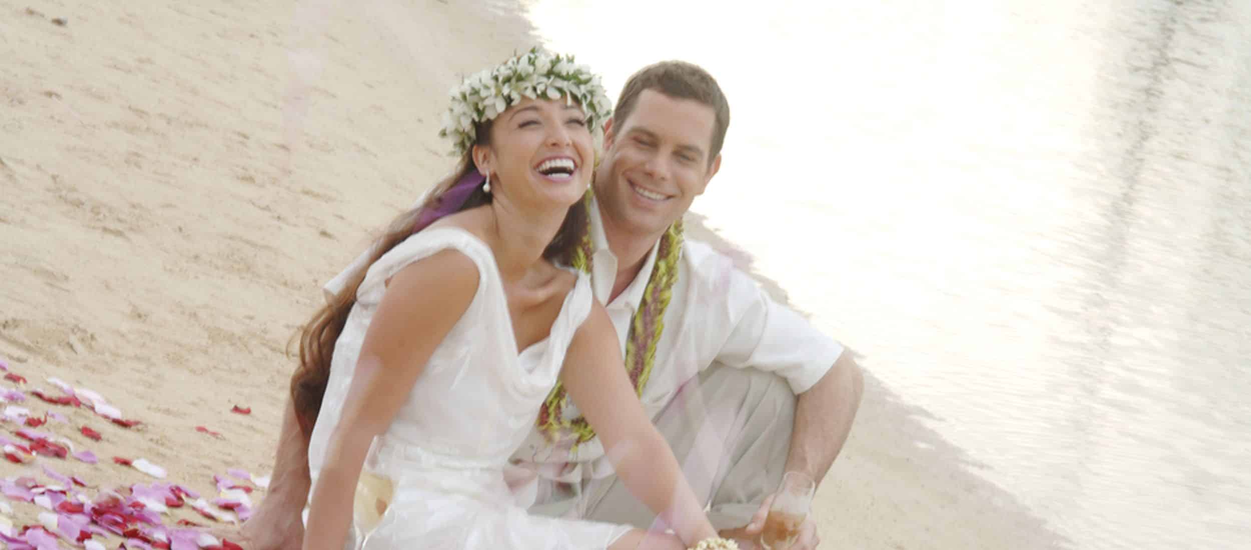Wedding couple sitting on sand with rose petals