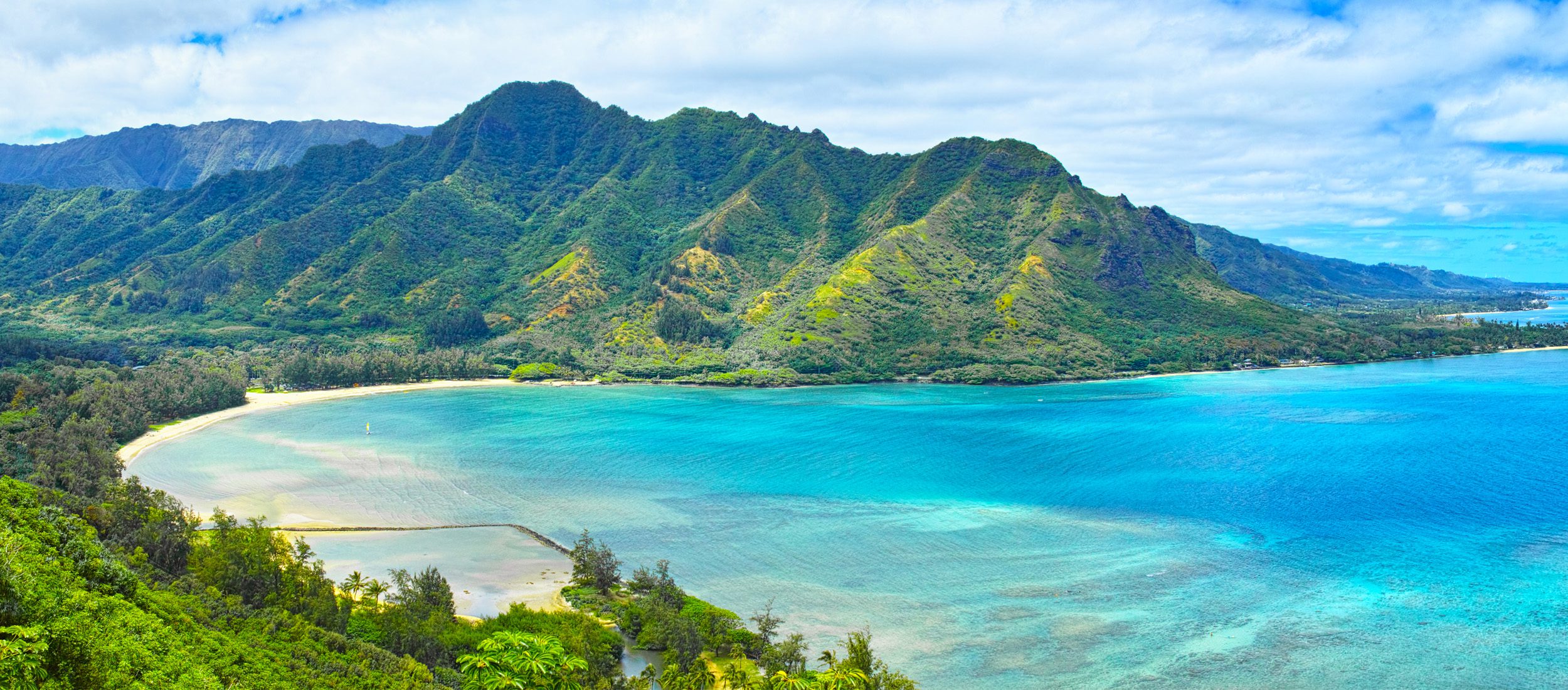 Scenic view on Oahu of beautiful Kahana Bay with blue water and green mountains along a coastline