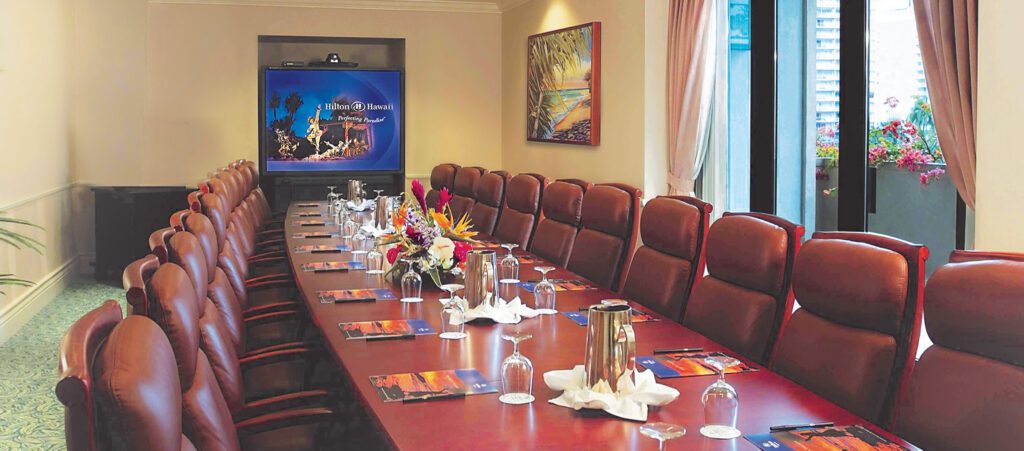 Ilima Boardroom at Kalia Conference Center. Close up of boardroom table set for an executive meeting with glassware and water canisters and television screen in background