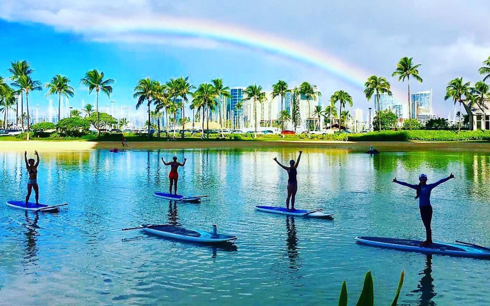 Stand Up Paddle Boarders on the Duke Kahanamoku Lagoon under a rainbow in the sky