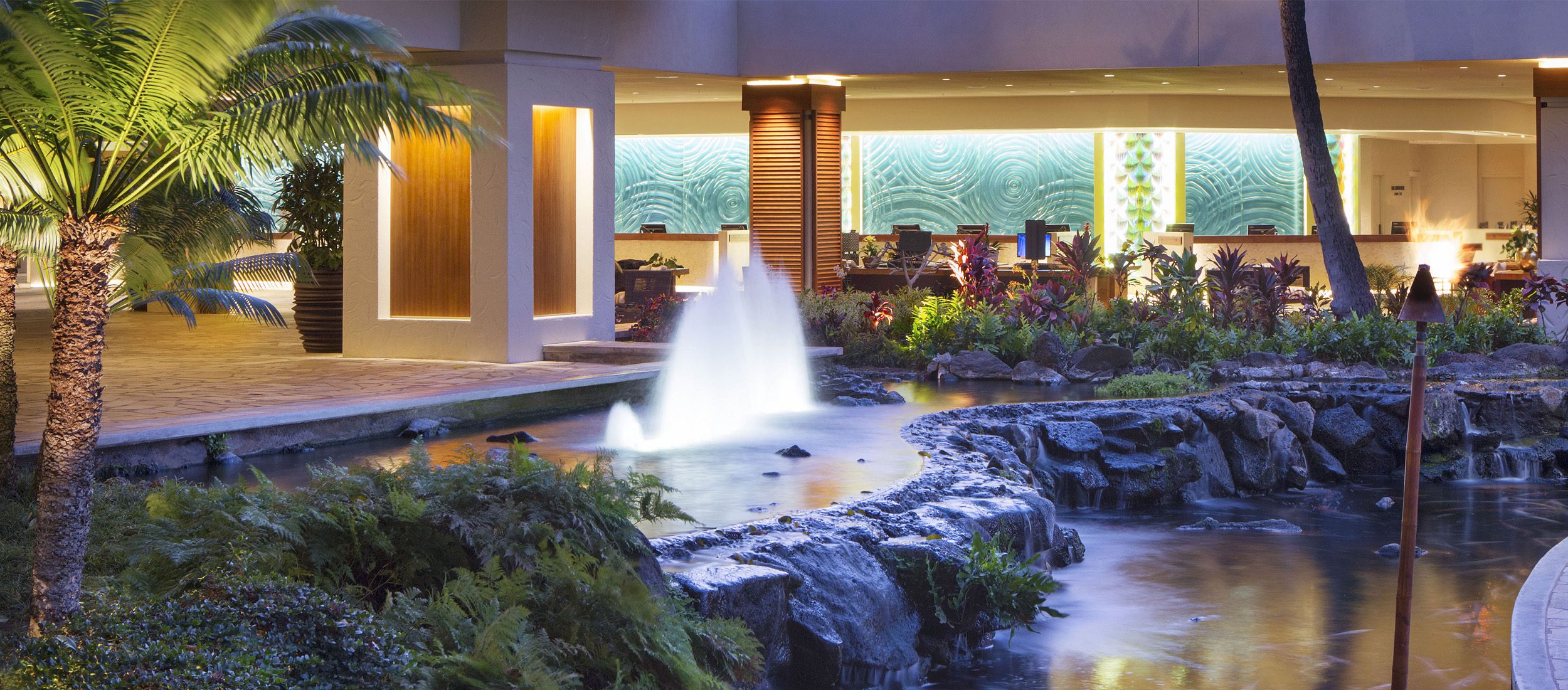 Hilton Hawaiian Village open air lobby with fountains and ponds. Blue wave glass on the back of the check-in desk.