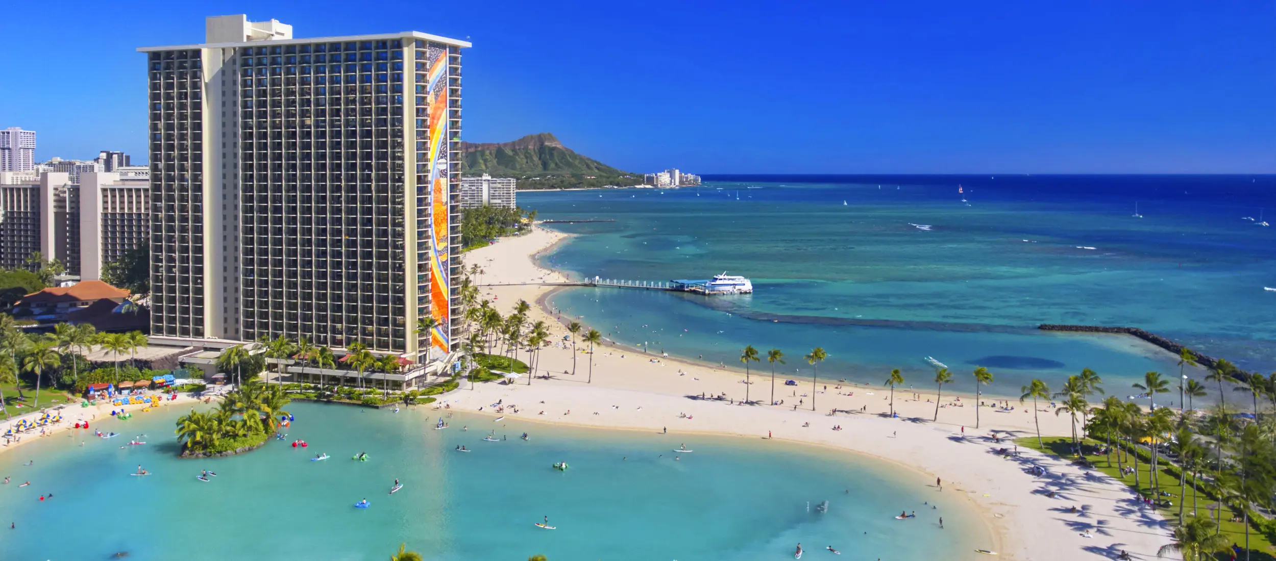 Rainbow Tower on Waikiki Beach with blue skies and blue ocean and the Duke Kahanamoku Lagoon in foreground